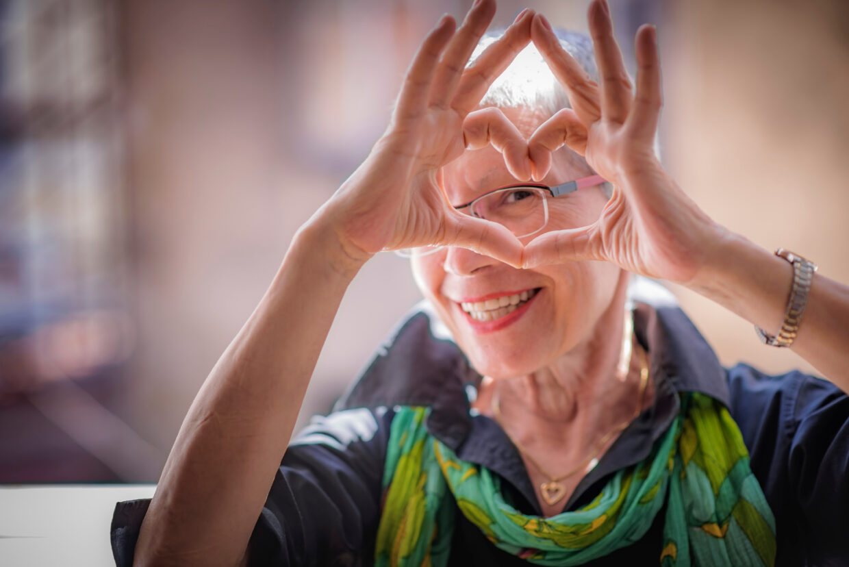 Cute senior old woman making a heart shape with her hands and fi