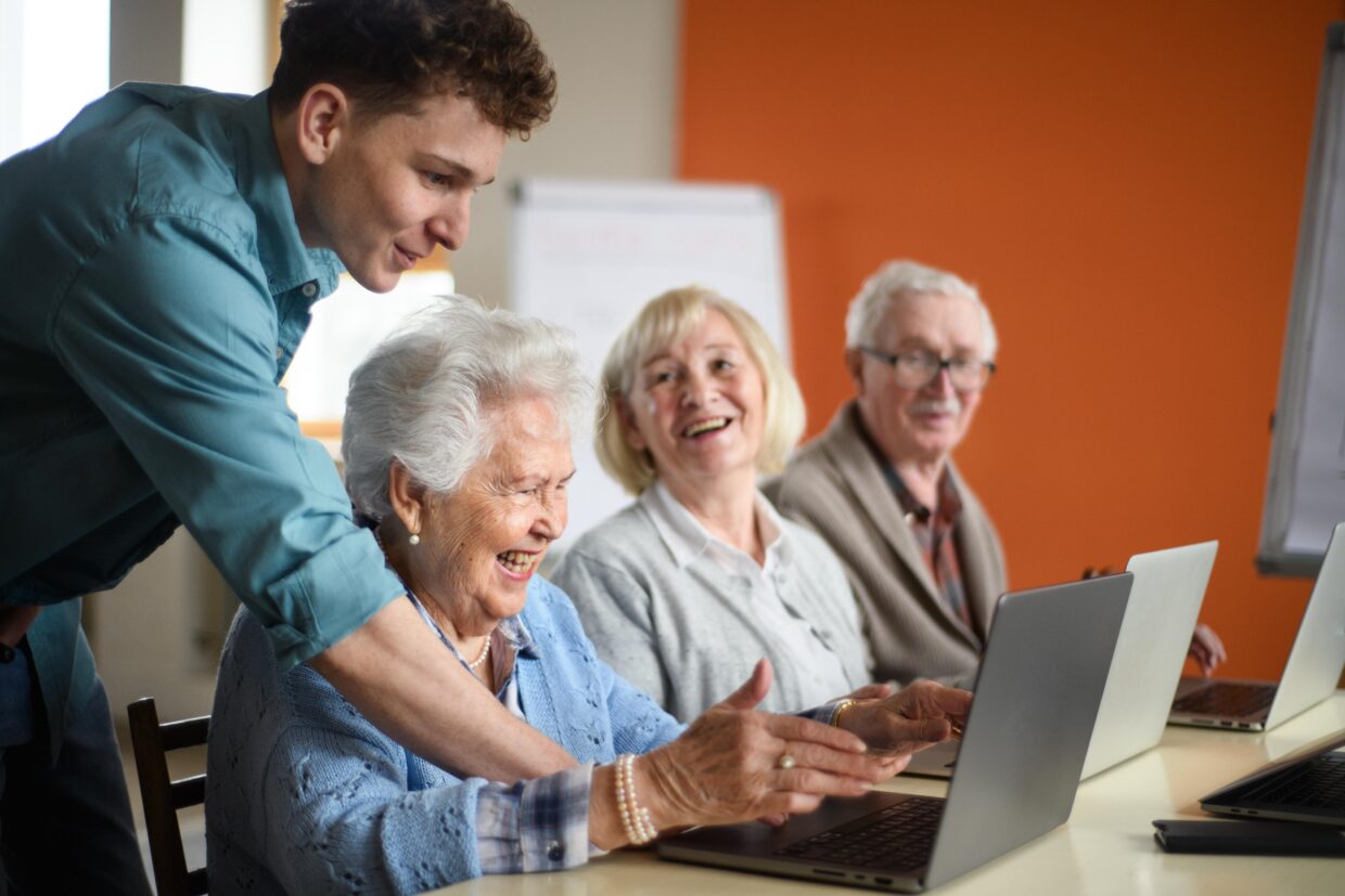 Senior group in retirement home with young instructor learning together in computer class